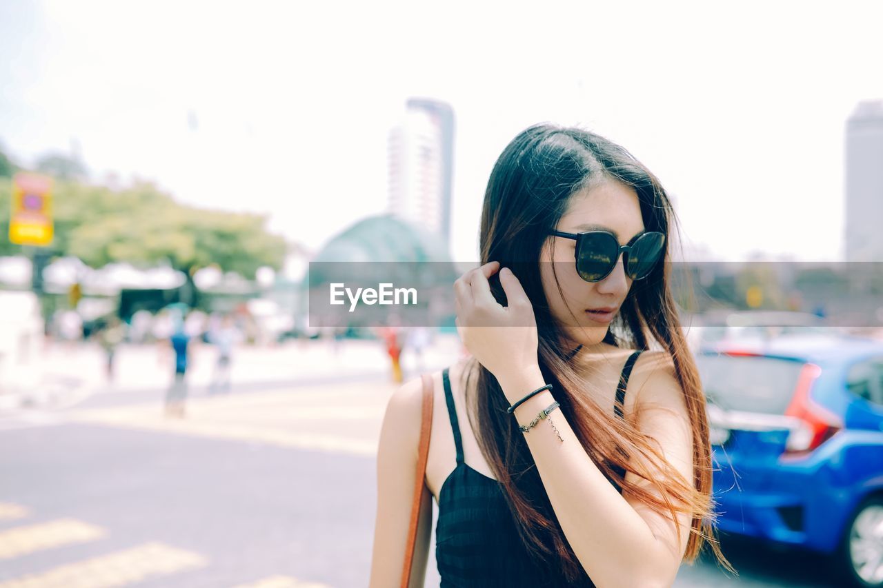 Beautiful young woman with hand in hair standing on street