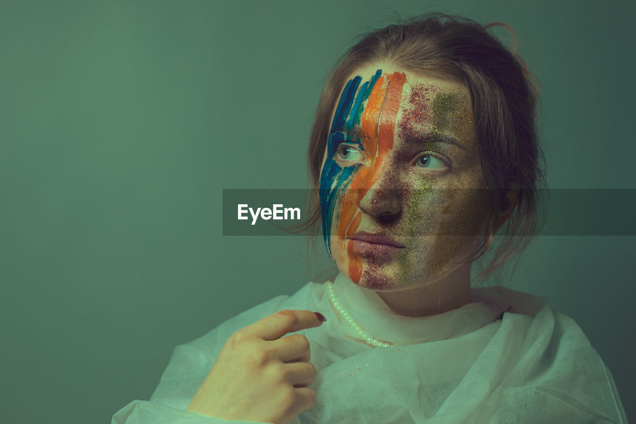 Young woman with painted face against green background