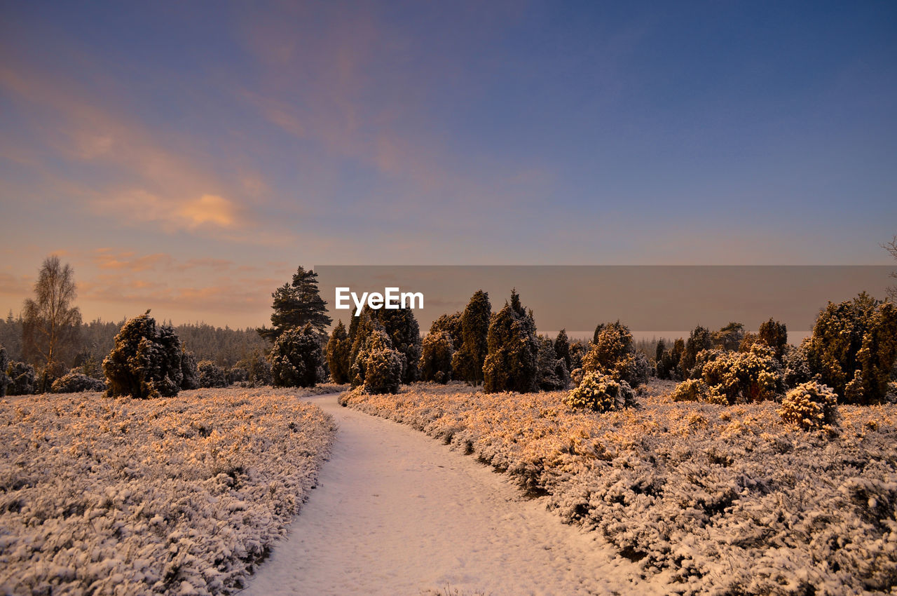 Snow covered landscape against sky during sunset