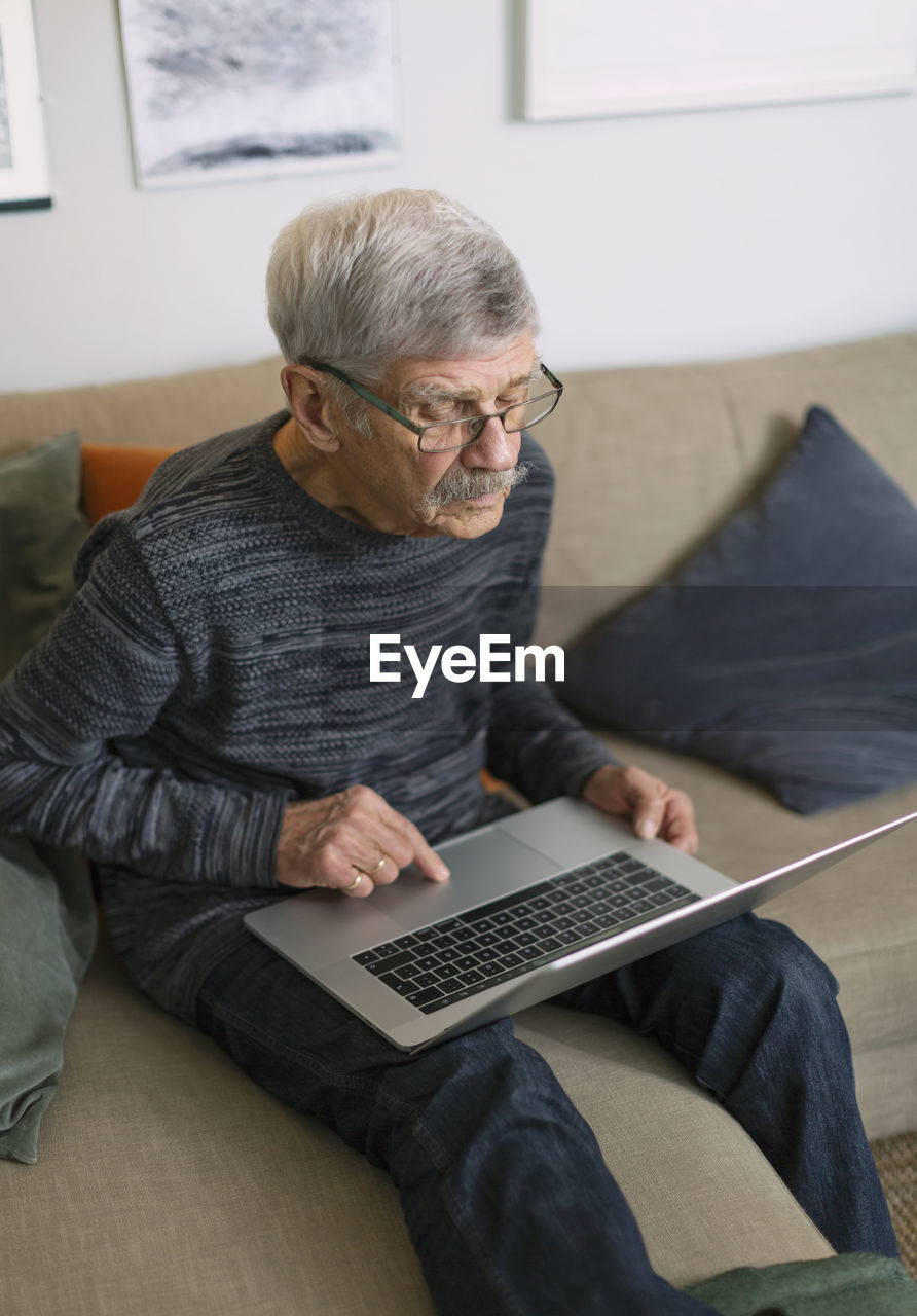 Senior man using laptop on sofa