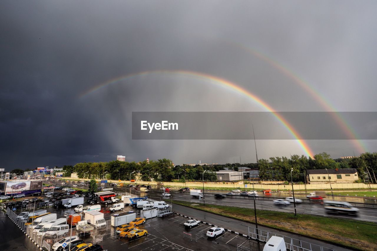 RAINBOW OVER ROAD IN CITY AGAINST SKY