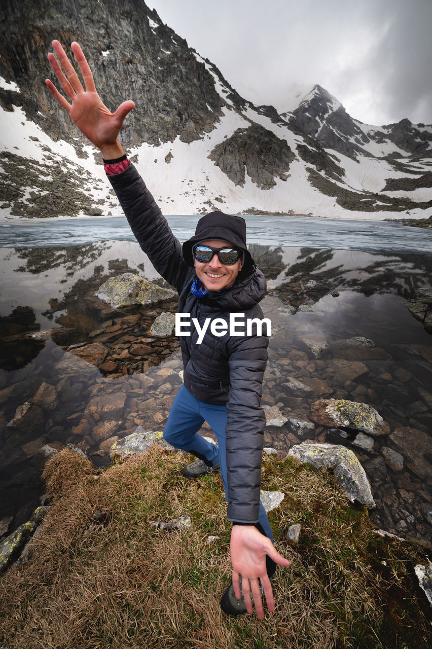 Handsome young man opens his hands outdoors. happy tourist standing in front of mountains, nature