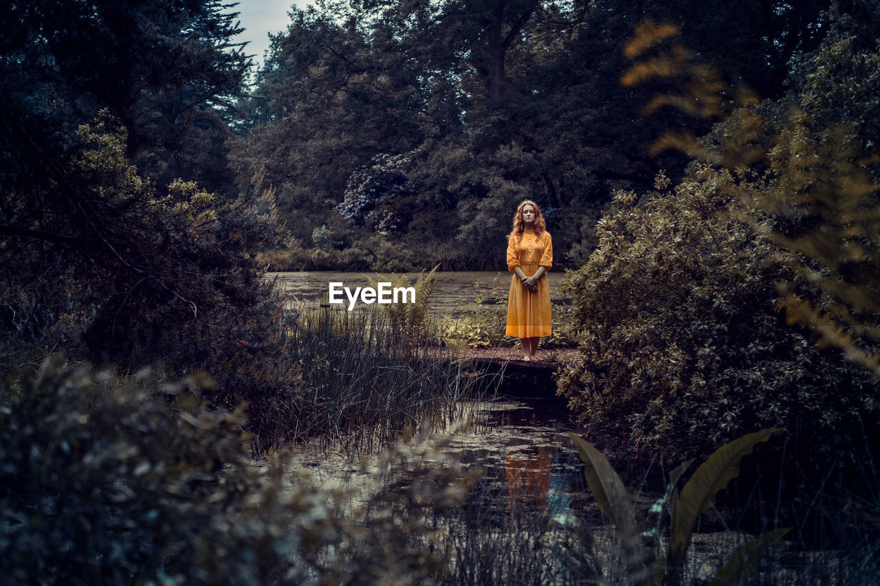 Portrait of young woman standing on field in forest