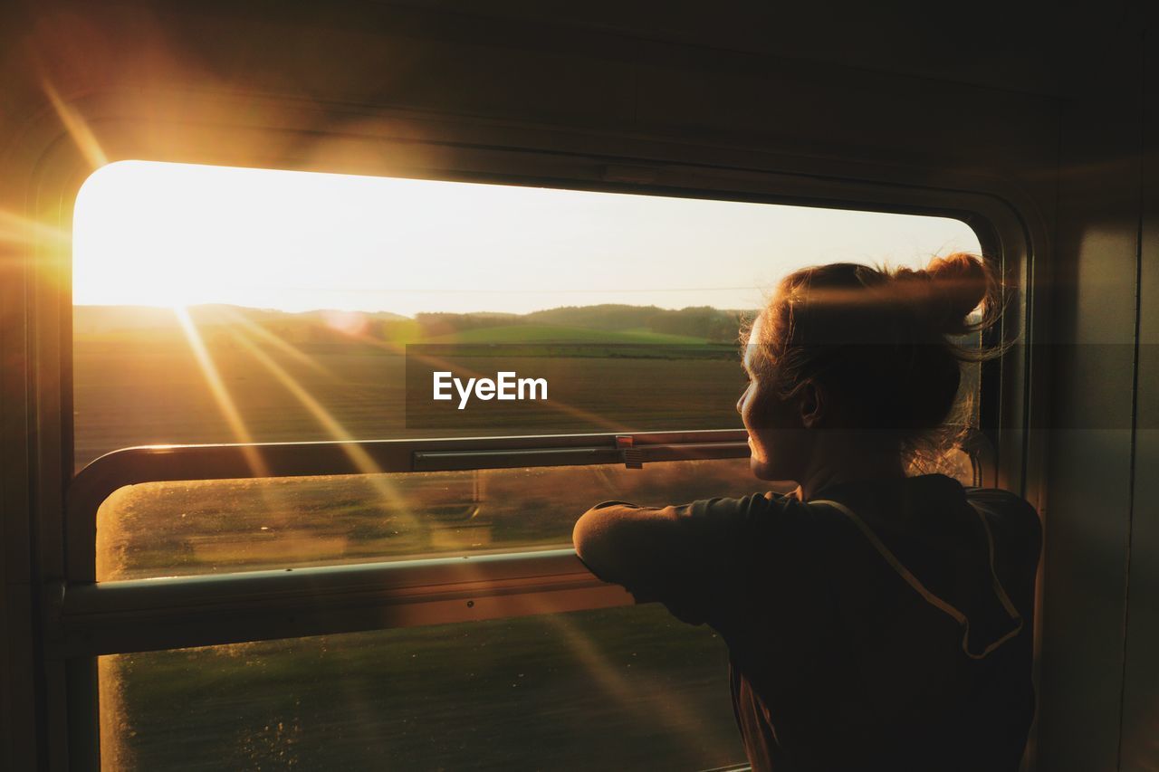 Young woman looking through window while traveling in train during sunset