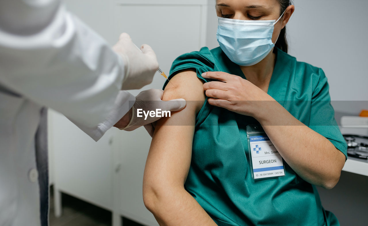 Midsection of doctor vaccinating patient in clinic