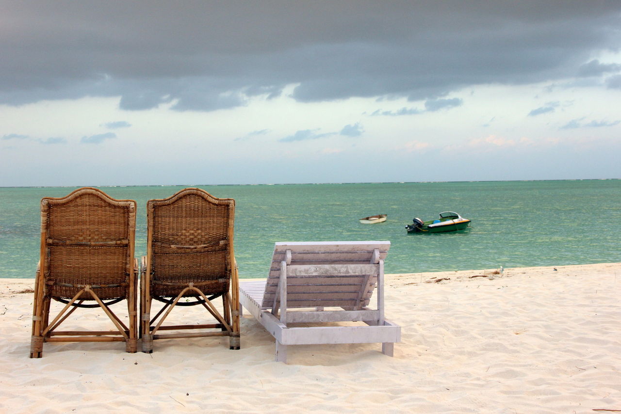 Deck chair on sand at beach against sky