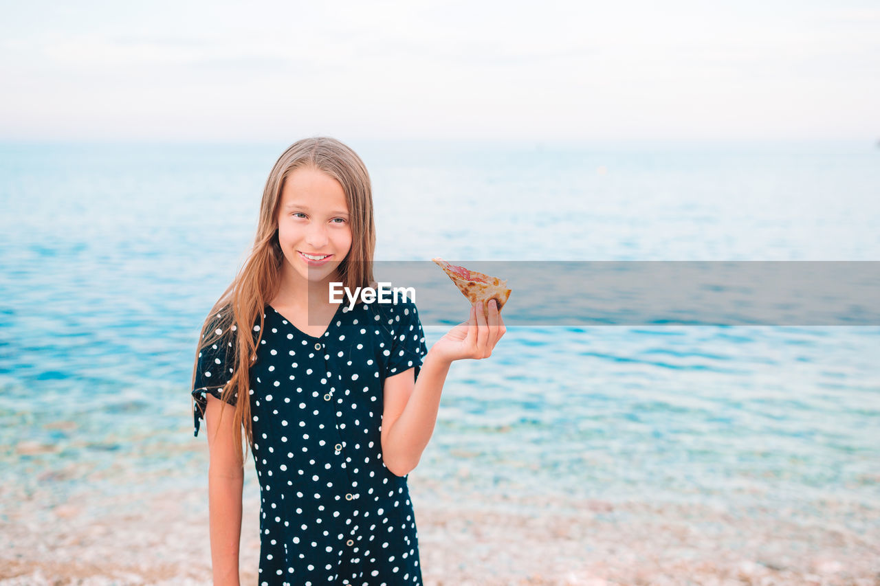 SMILING YOUNG WOMAN STANDING ON BEACH