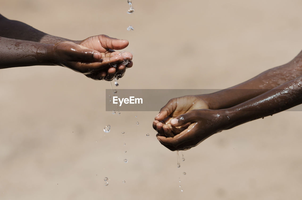 CROPPED IMAGE OF HAND TOUCHING WATER SPLASHING AGAINST SKY