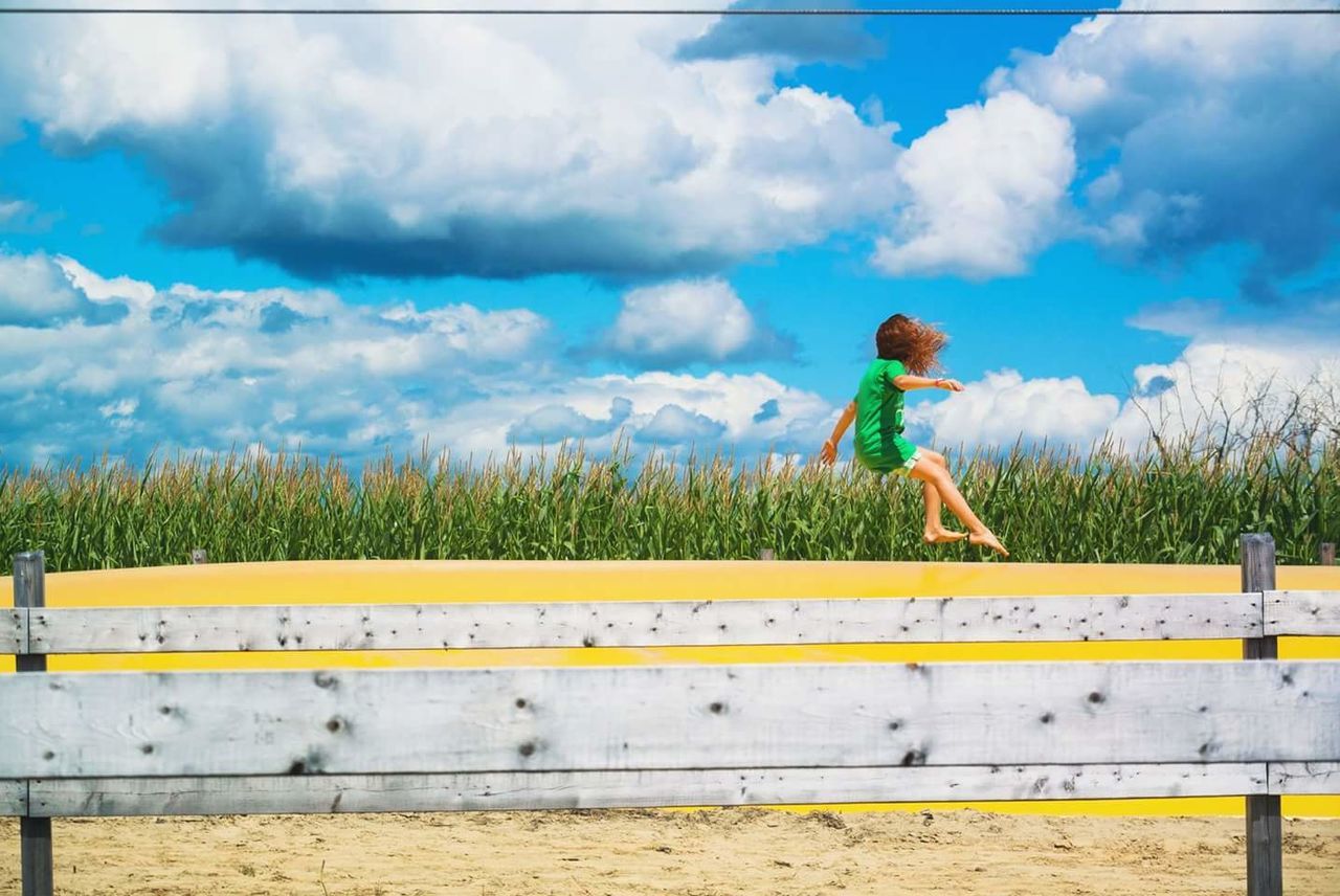 Full length of children jumping over wooden fence against cloudy sky