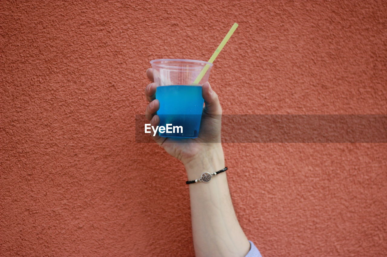 Close-up of hand holding drink against wall