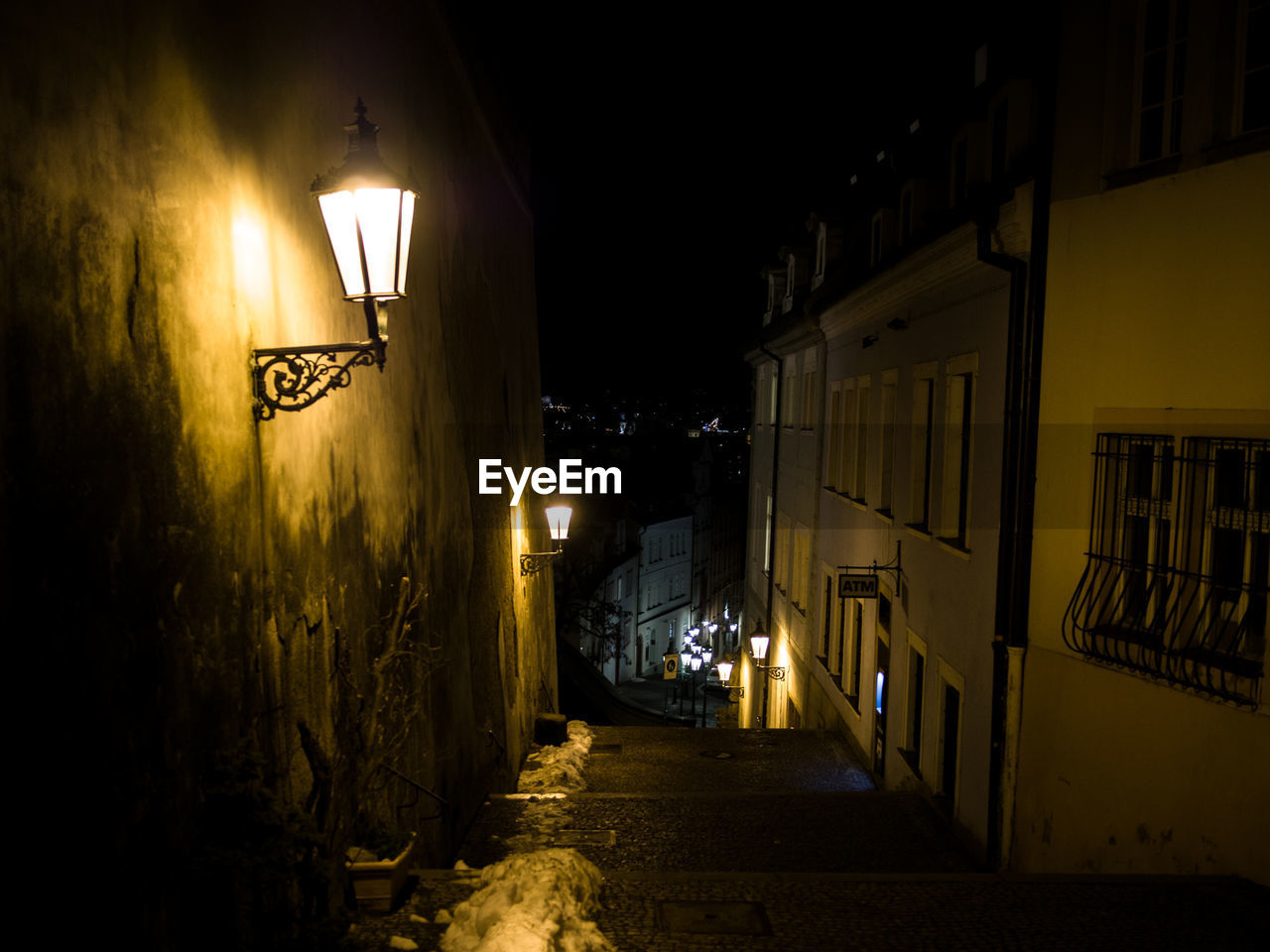 Illuminated street light on alley amidst buildings at night