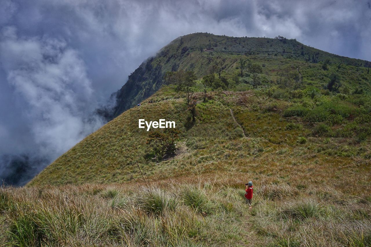 REAR VIEW OF MAN STANDING ON MOUNTAIN