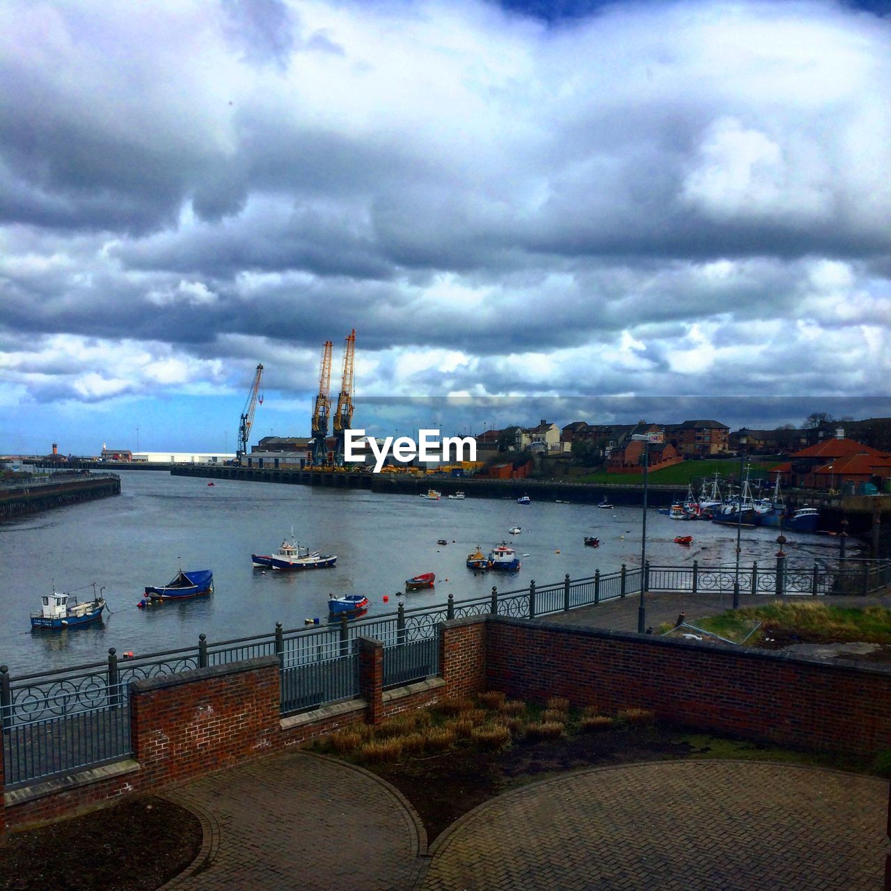 BOATS MOORED AT HARBOR AGAINST CLOUDY SKY