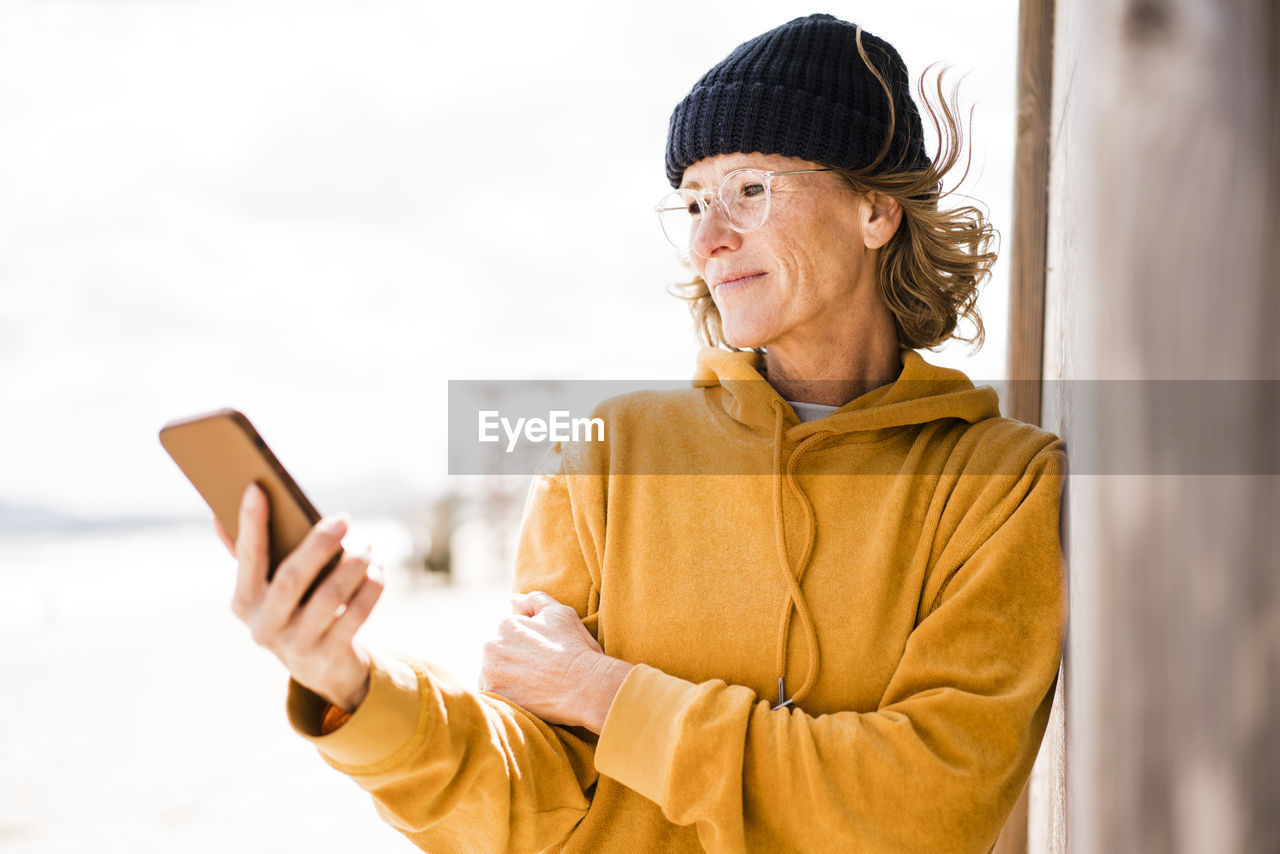 Smiling mature woman wearing eyeglasses using smart phone