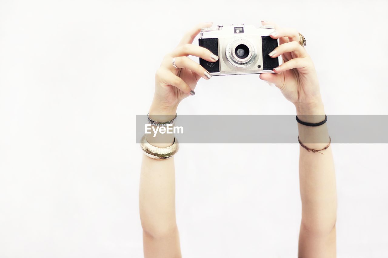 Cropped hands of woman photographing against white background