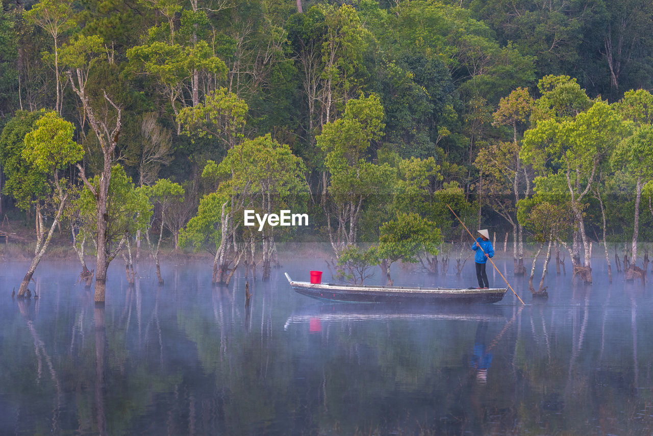 PEOPLE IN BOAT BY TREES IN FOREST