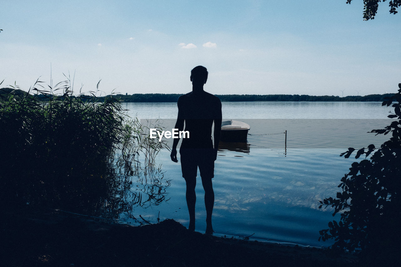 Silhouette man standing by lake against sky