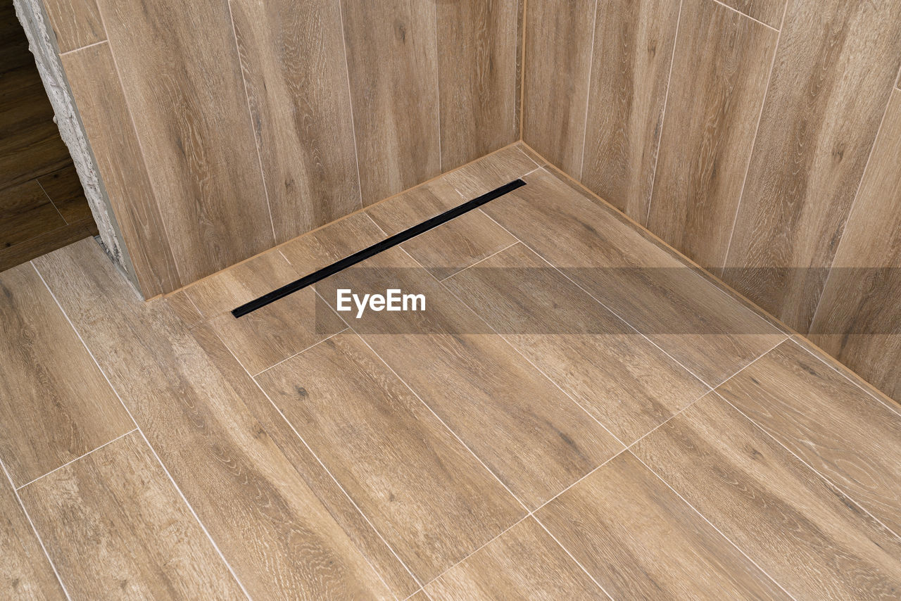 Modern black linear drain in a bathroom lined with ceramic tiles imitating wood.