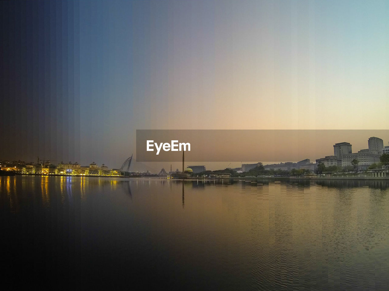 REFLECTION OF ILLUMINATED BUILDINGS IN WATER AT SUNSET