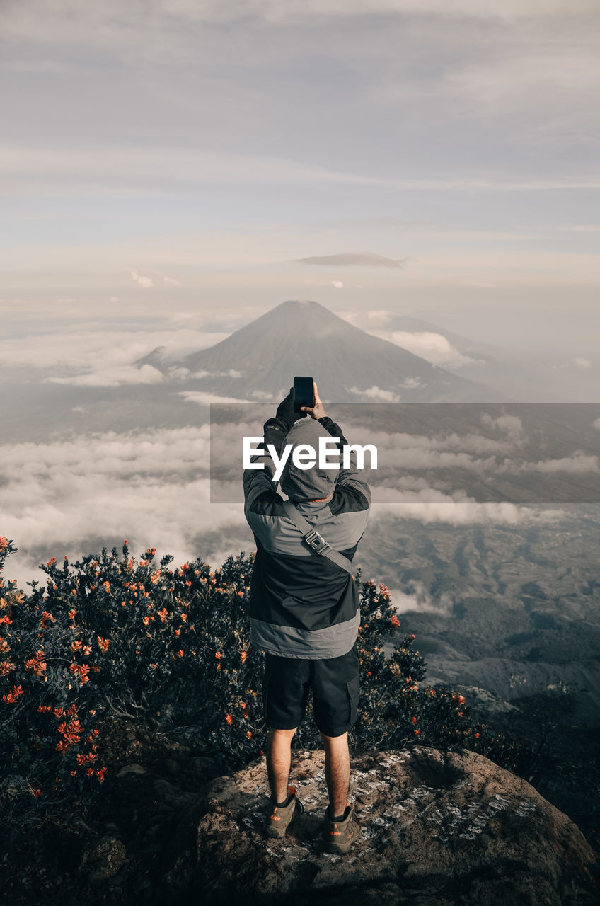 REAR VIEW OF MAN STANDING AGAINST MOUNTAIN