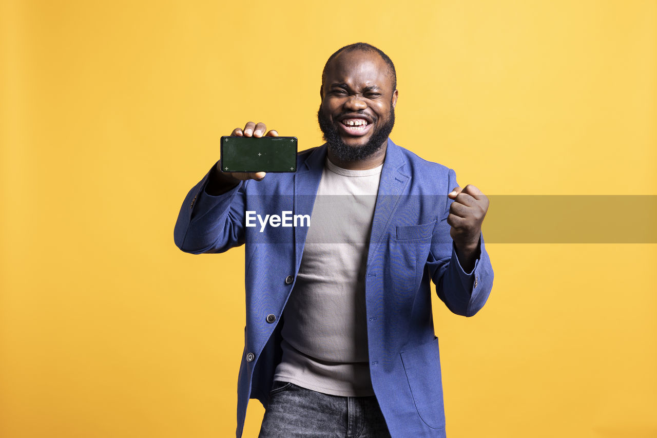 portrait of young man with smart phone against yellow background