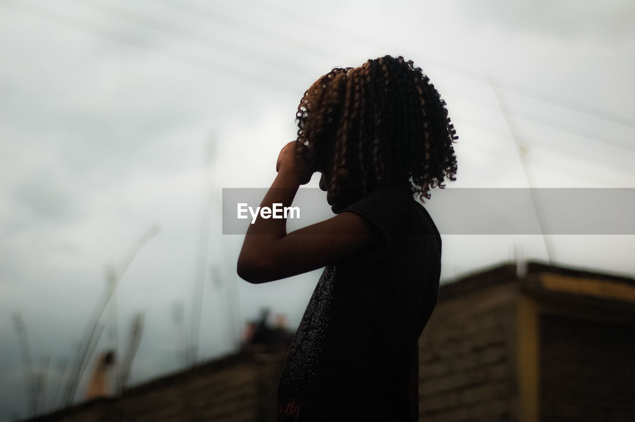 Girl with curly hair standing against sky