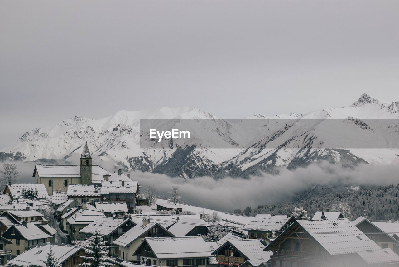 Scenic view of snowcapped mountains in front 8of houses against clear sky during winter