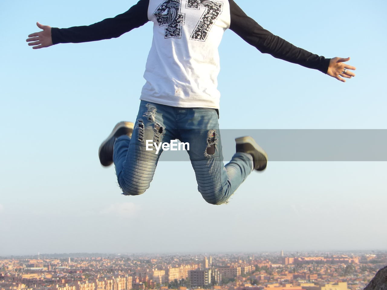 Low section of man jumping over city against sky