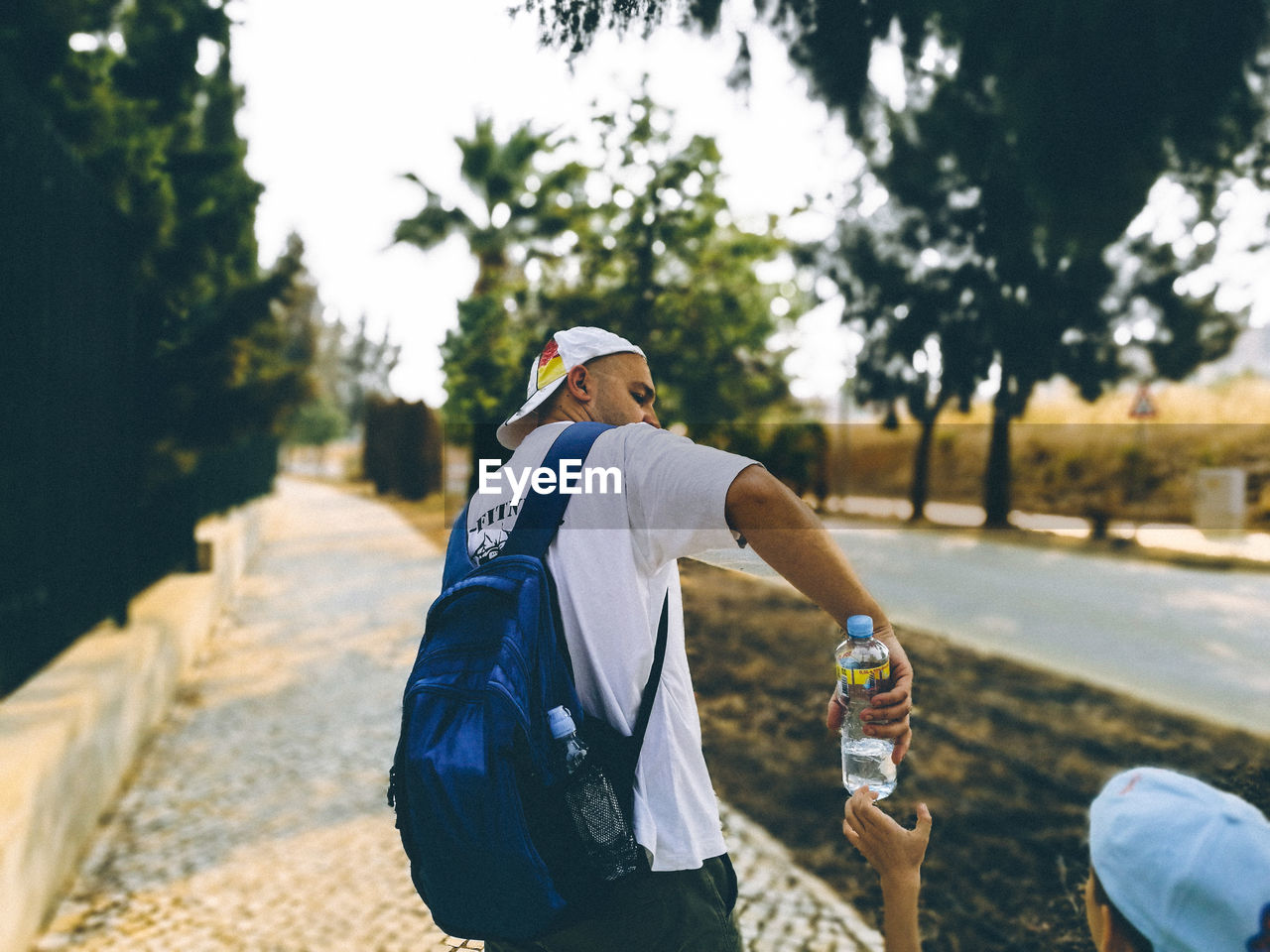 Mid adult man giving water bottle to son on sidewalk