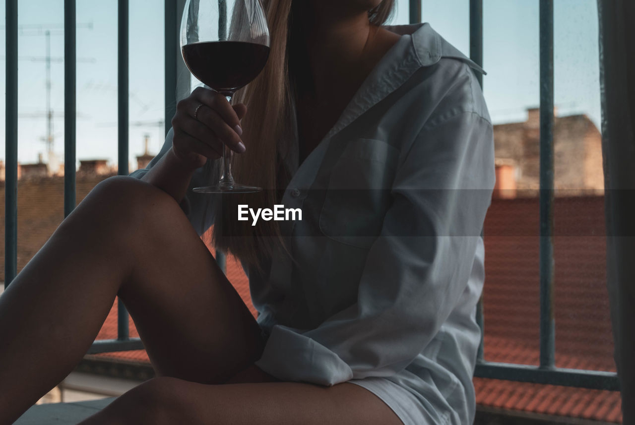 Midsection of woman holding wineglass while sitting against railing