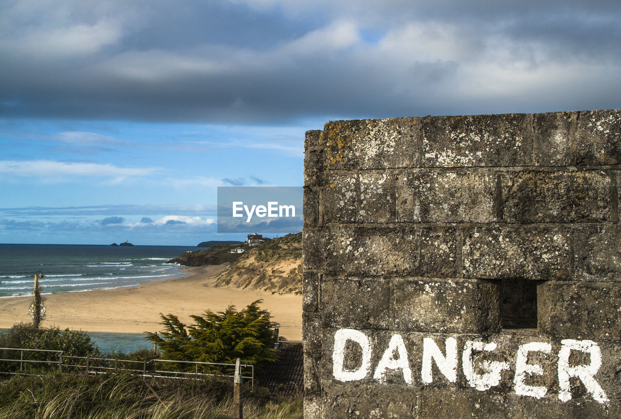 Danger sign on old wall at beach against sky