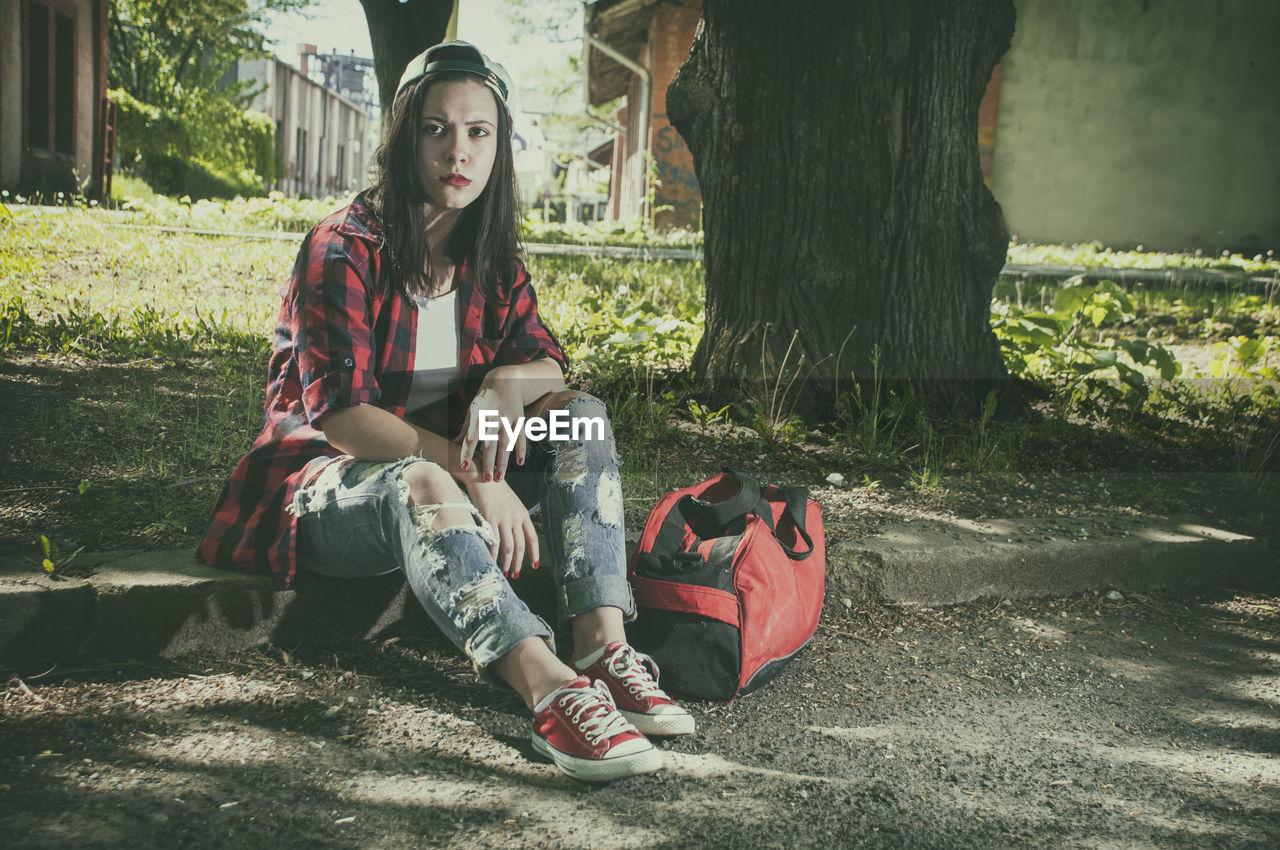 Young woman sitting by bag on field