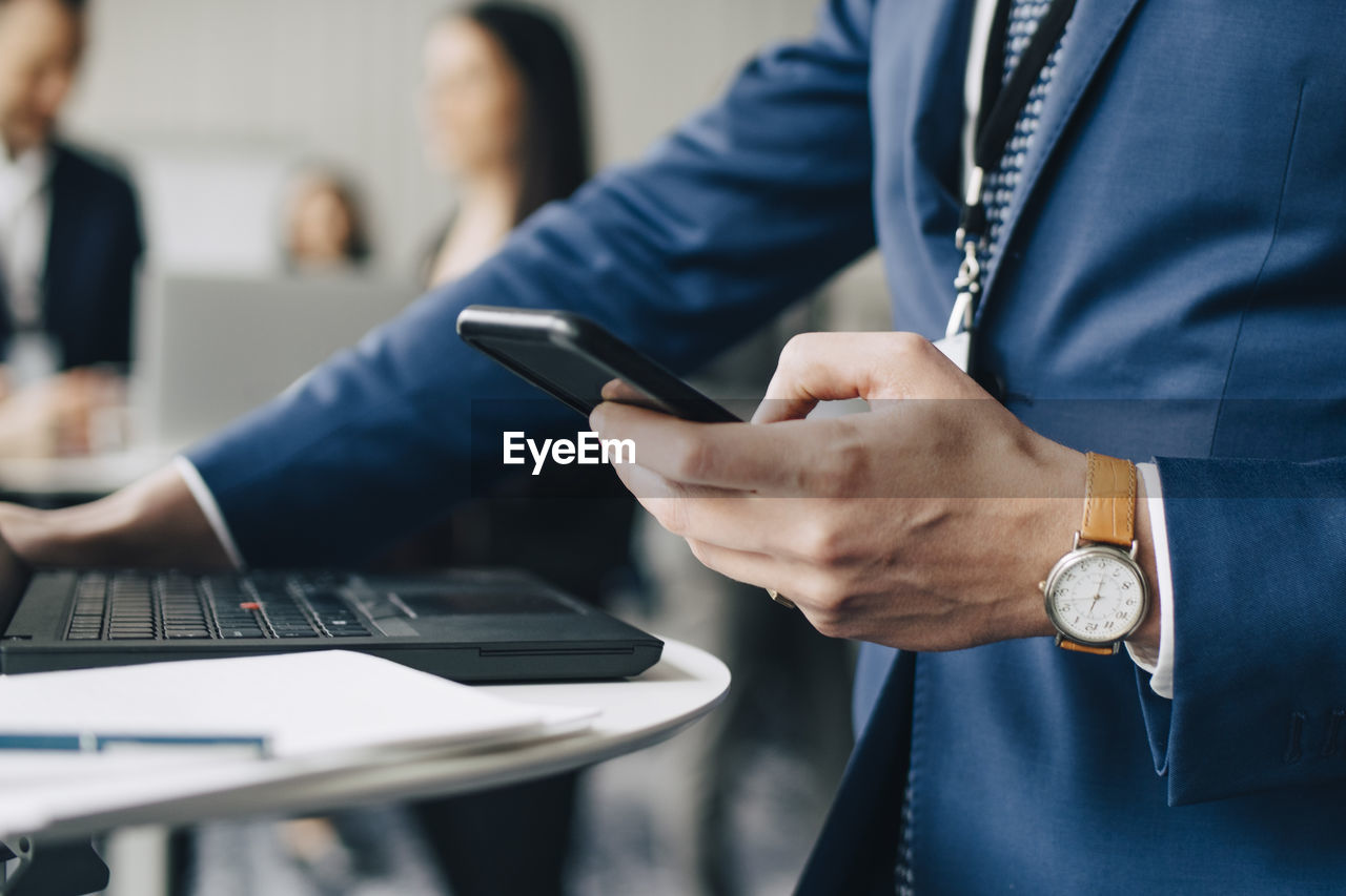 Midsection of businessman using phone while standing in office seminar