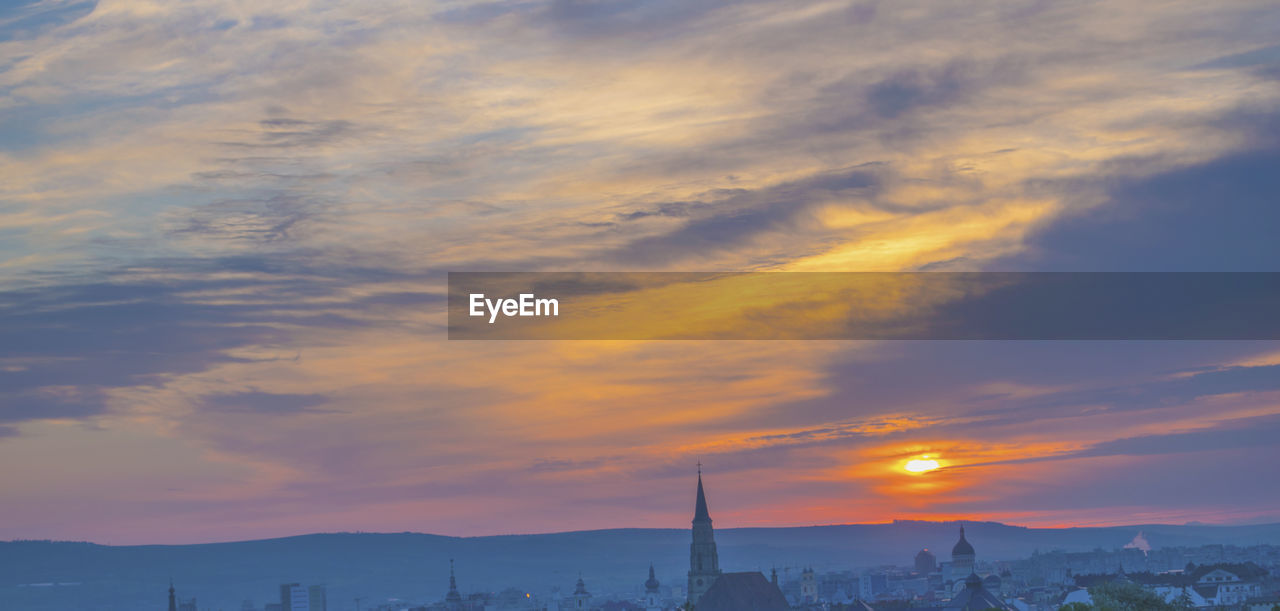 Cityscape against cloudy sky during sunset