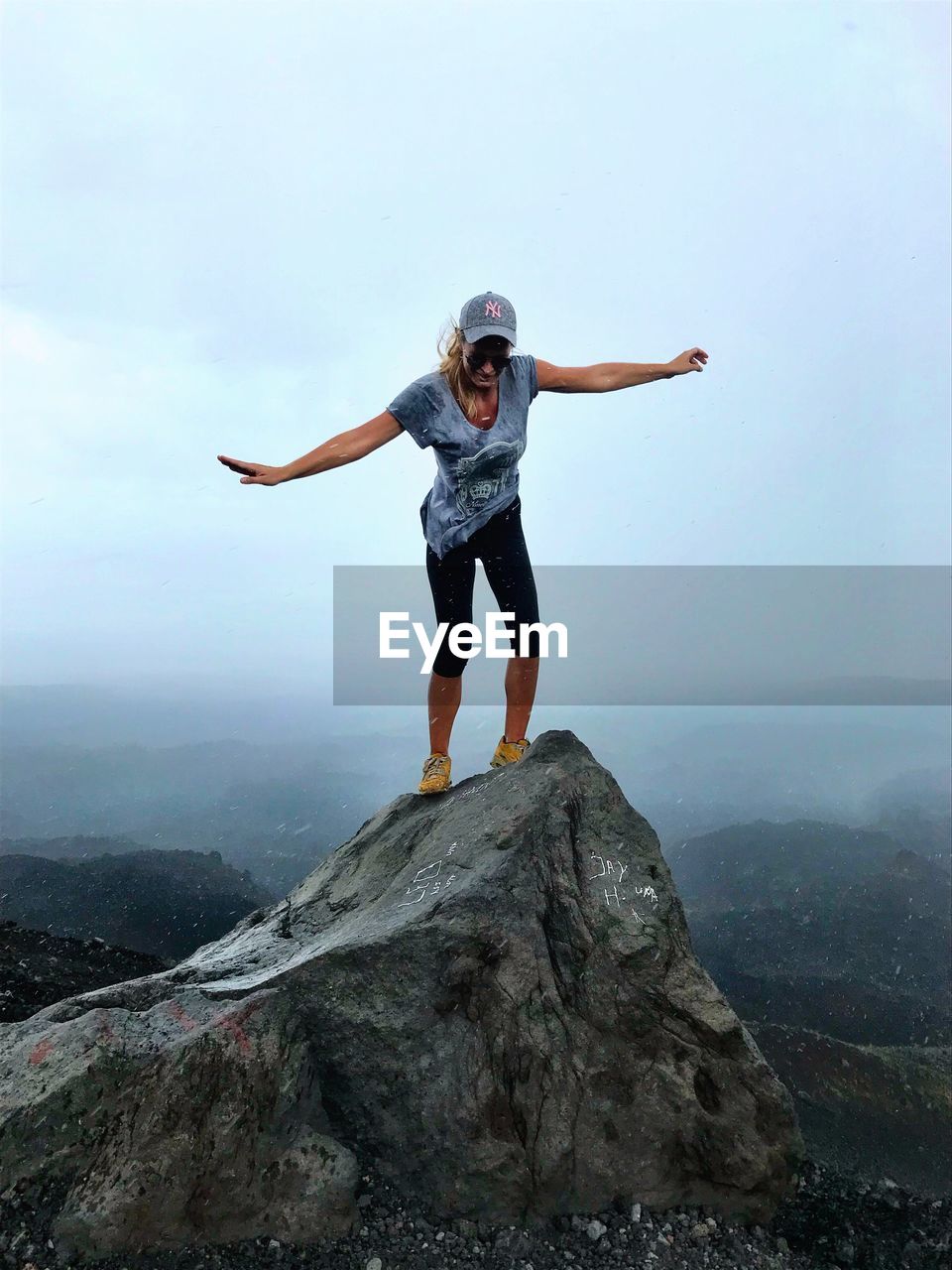Full length of mature woman standing on rock against cloudy sky
