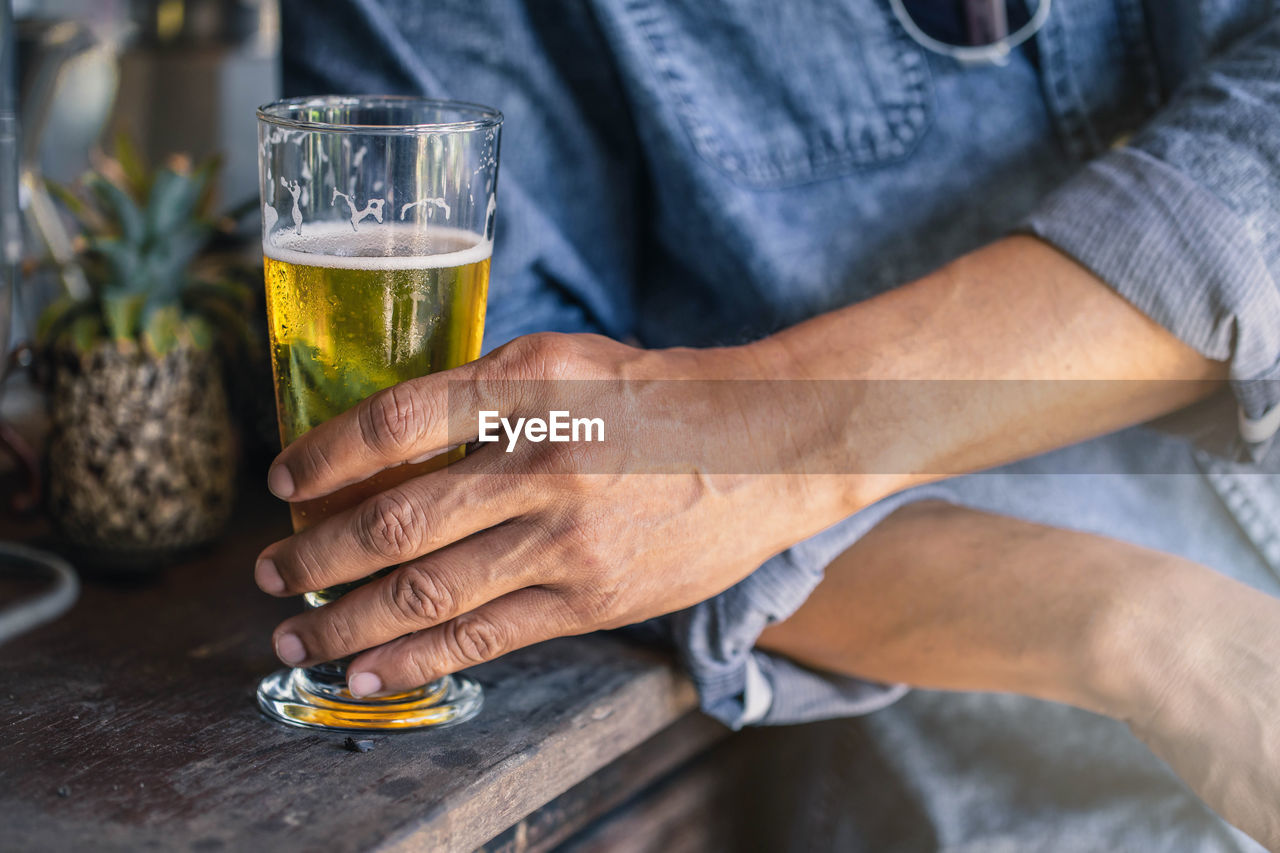 MIDSECTION OF MAN DRINKING GLASS WITH BEER ON TABLE