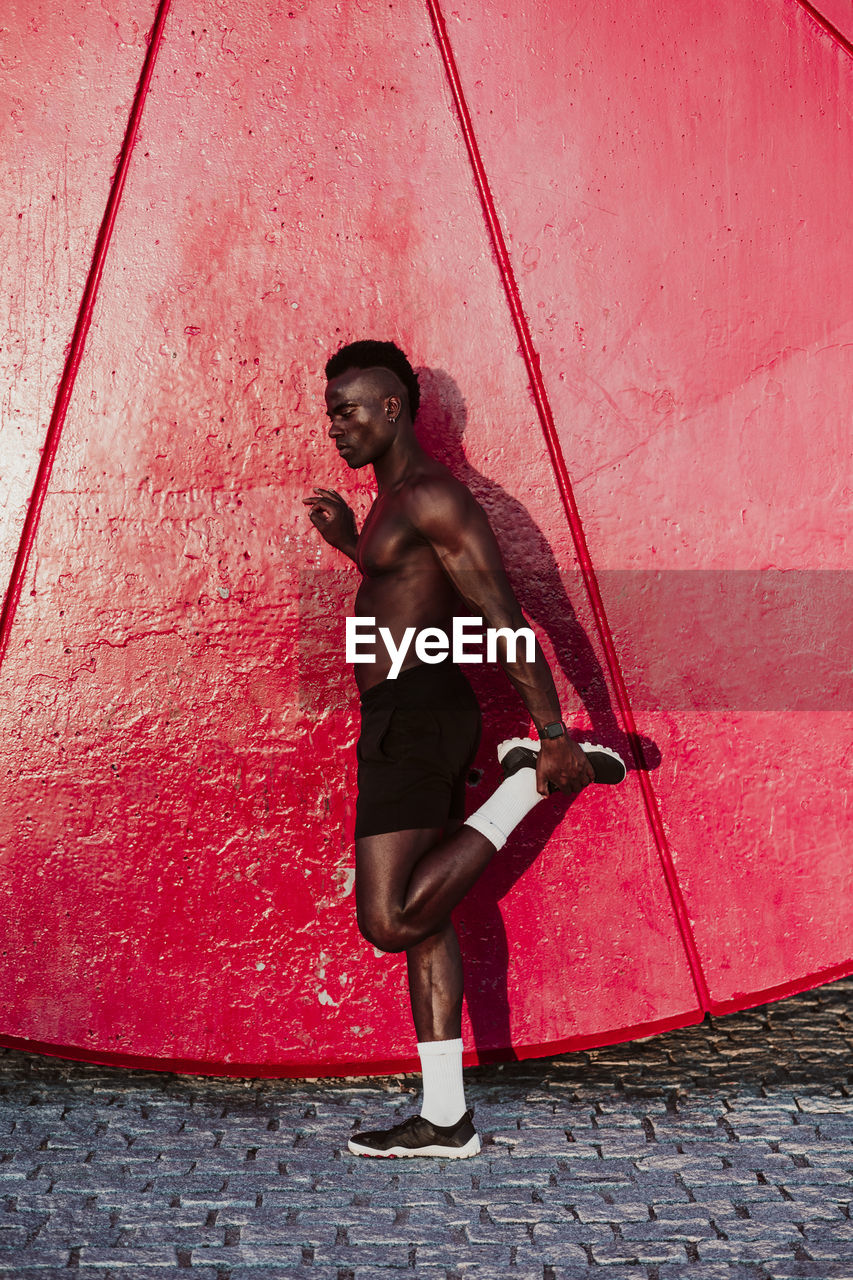 Male athlete with leg up standing by wall during sunset