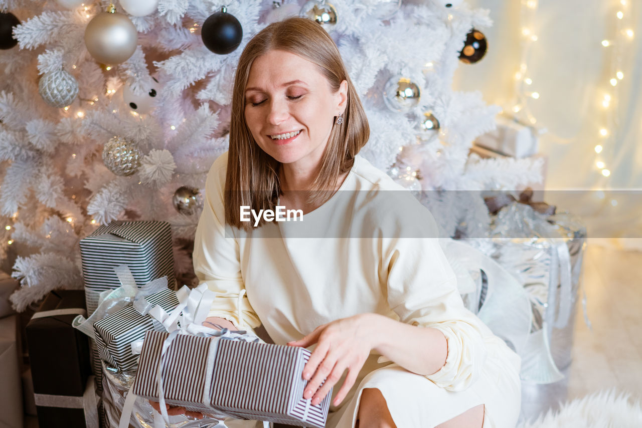 Smiling caucasian young woman opens box with christmas present. christmas