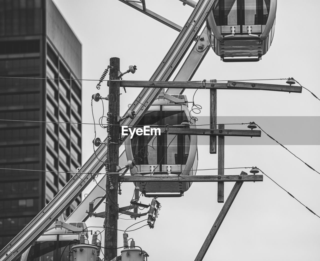 Low angle view of electricity pylon by ferris wheel against sky