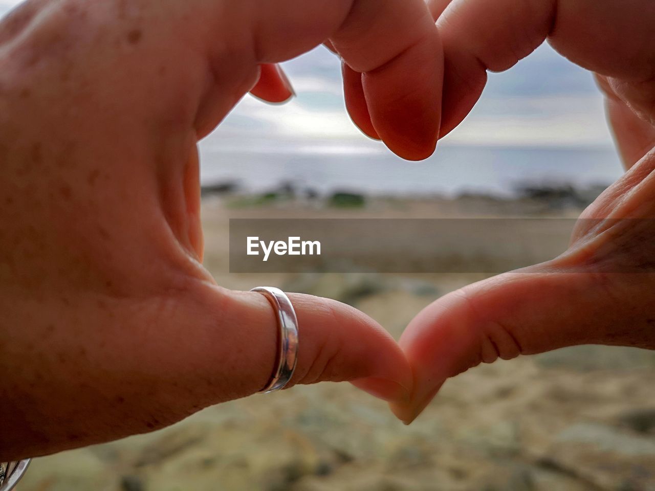 Cropped hands making heart shape at beach