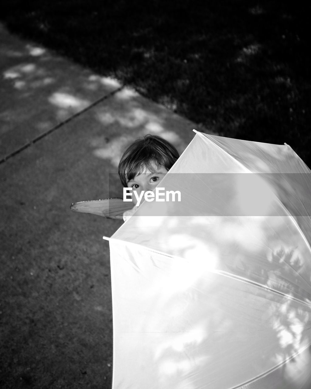 High angle portrait of girl holding umbrella while standing on footpath at park