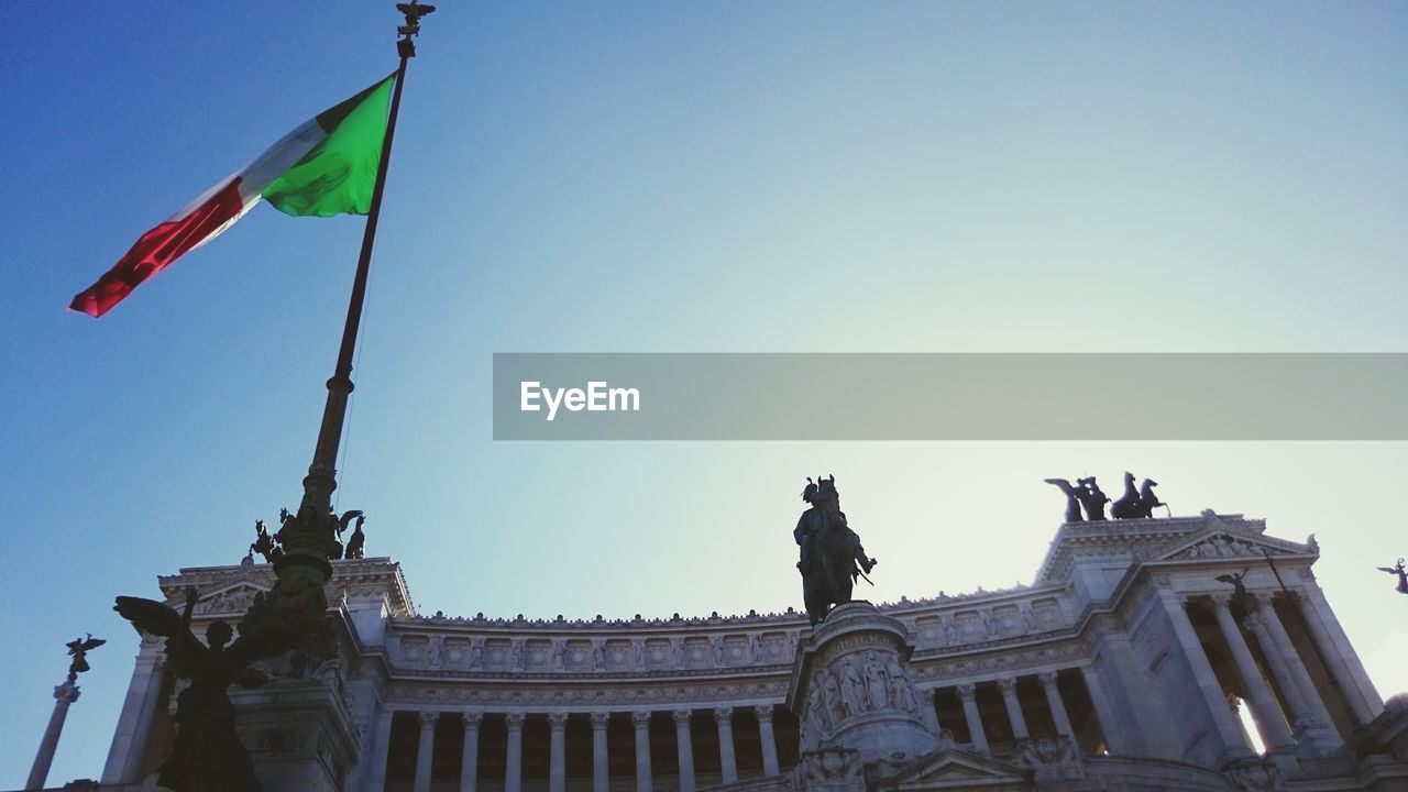 Low angle view of italian flag by altare della patria against clear sky