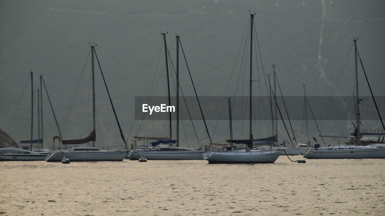 SAILBOATS MOORED AT SEA AGAINST SKY