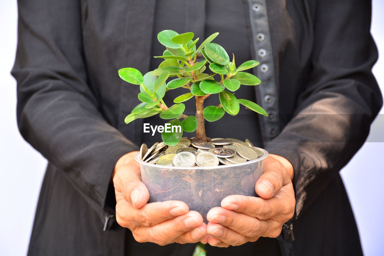 Midsection of man holding seedling in coins