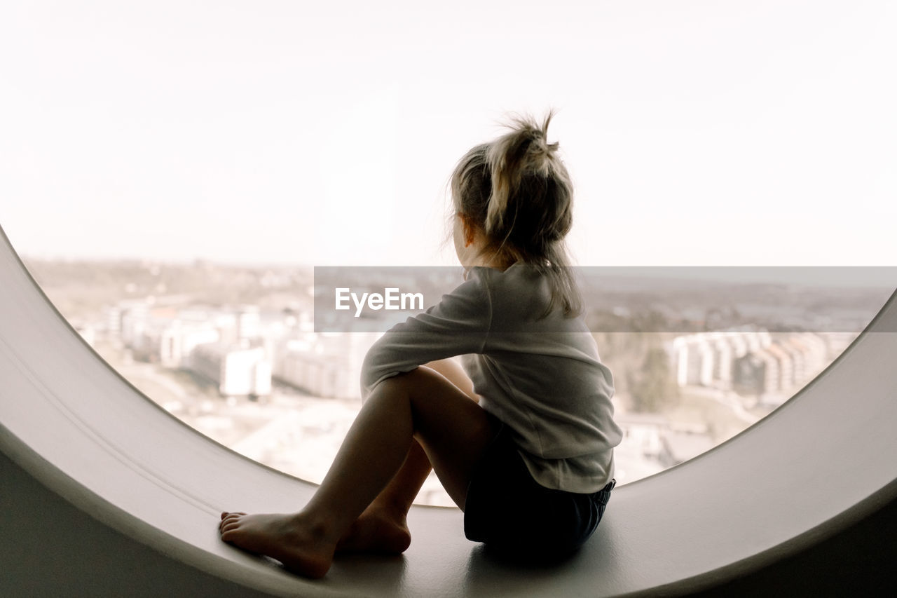 Full length of girl sitting on window sill in hotel room