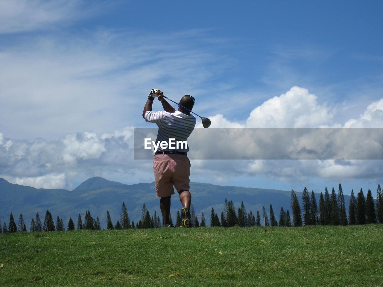 Rear view playing golf on grassy field against mountains and cloudy sky