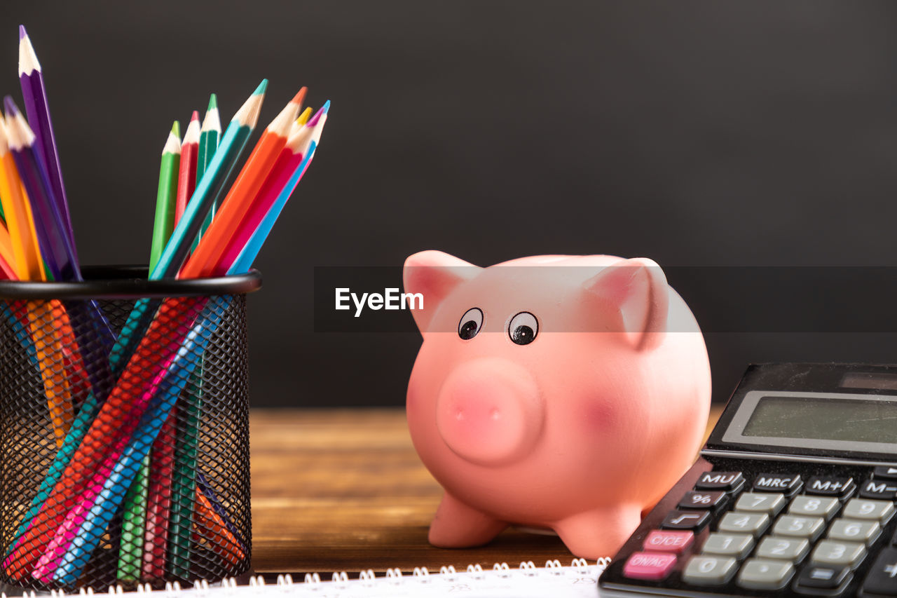 Close-up of piggy bank with school supplies on table against black background