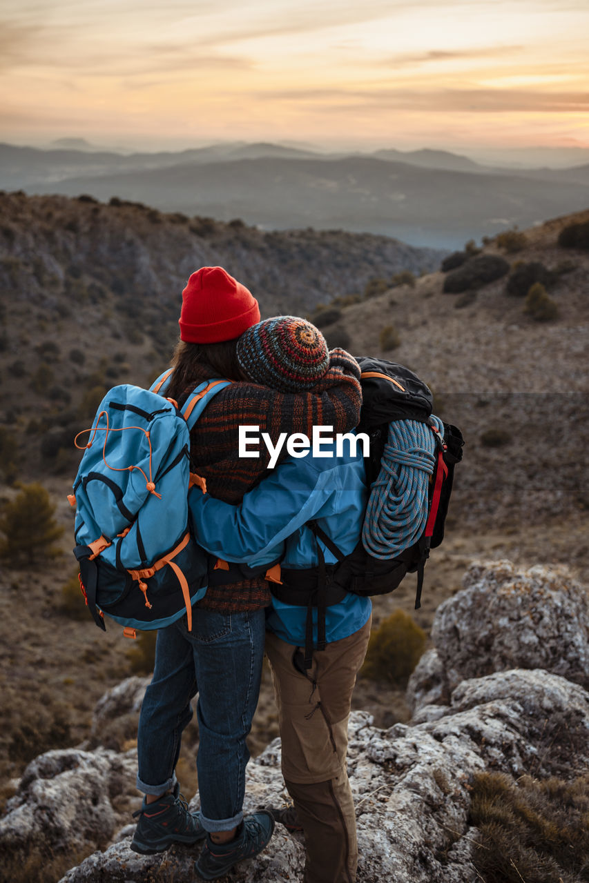 Couple embracing while standing on mountain peak during sunset