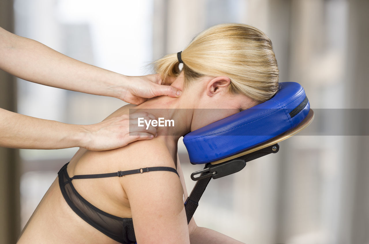 Cropped hands of young woman giving neck massage to mature woman on chair