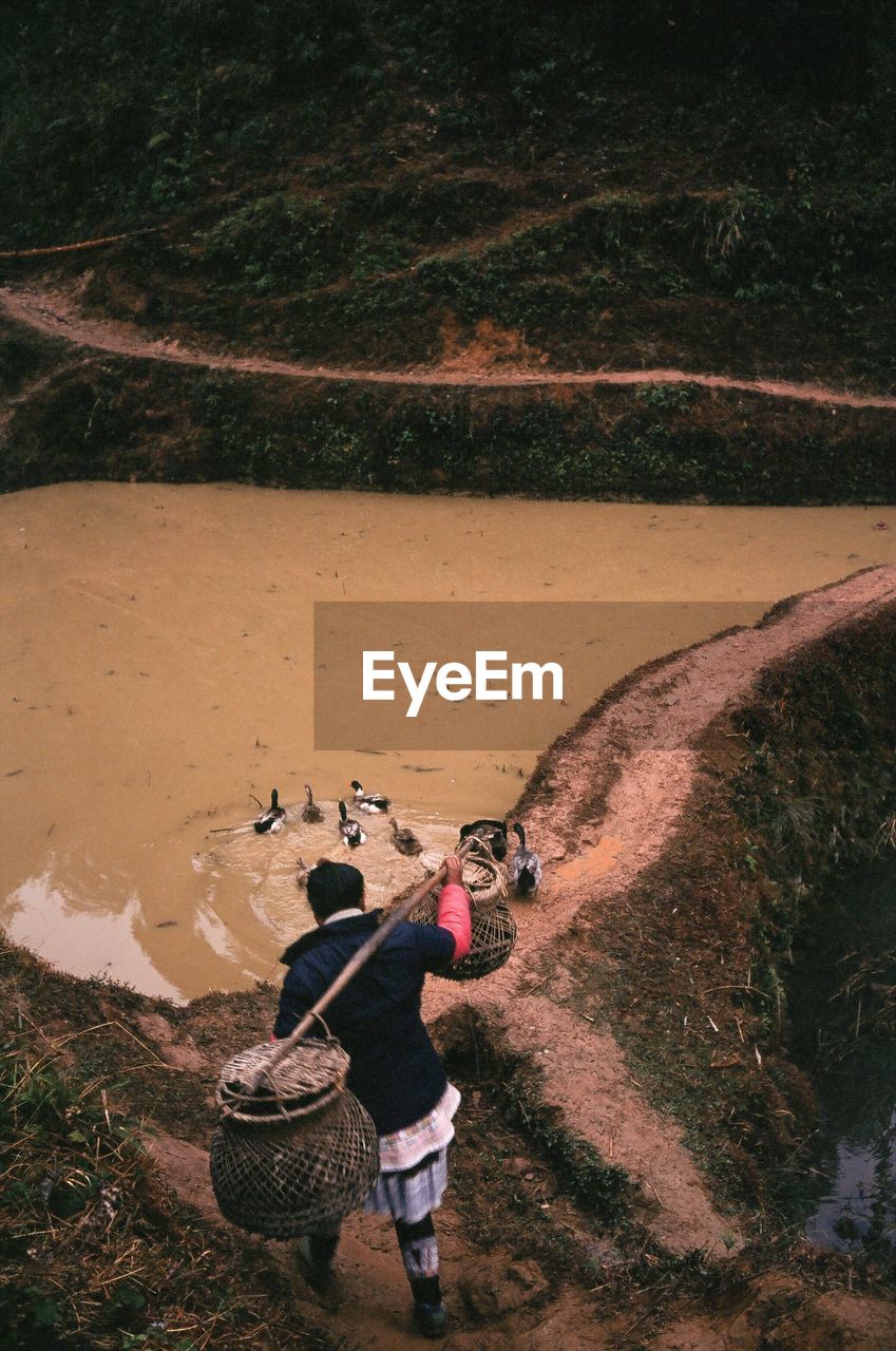 High angle view of man walking with baskets on land by lake